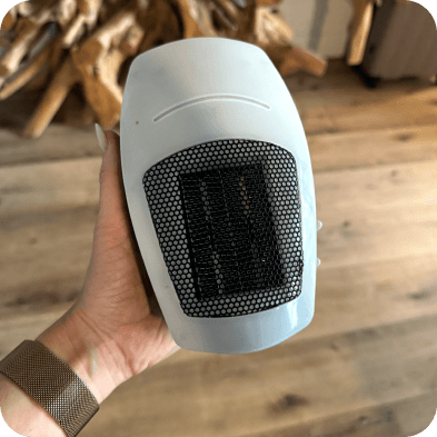 A hand holding a small white ceramic heater.